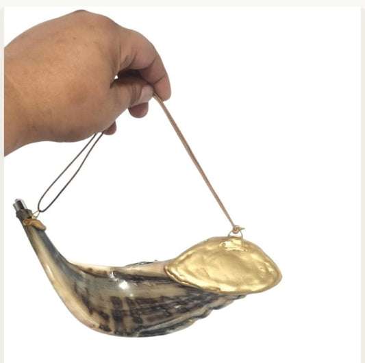Hand holding a ram's horn anointing oil vessel by its leather cord, showing the gold-tone lid